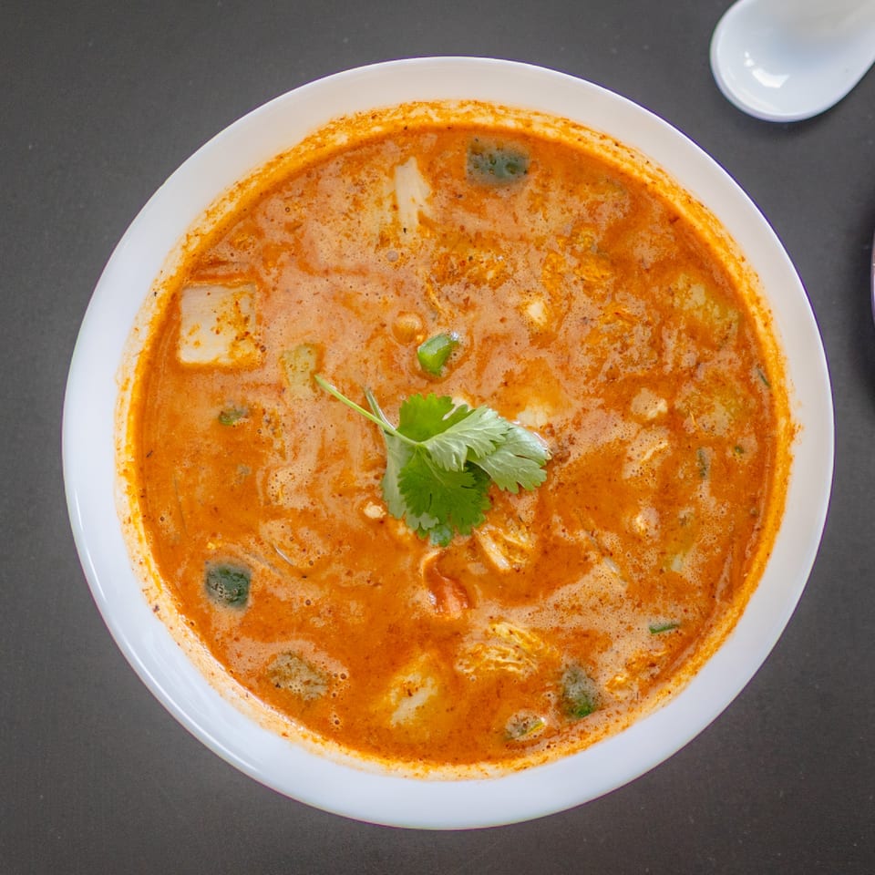 Overhead view of a bowl of orange-red soup with cilantro garnish, from Lover's Eggroll.