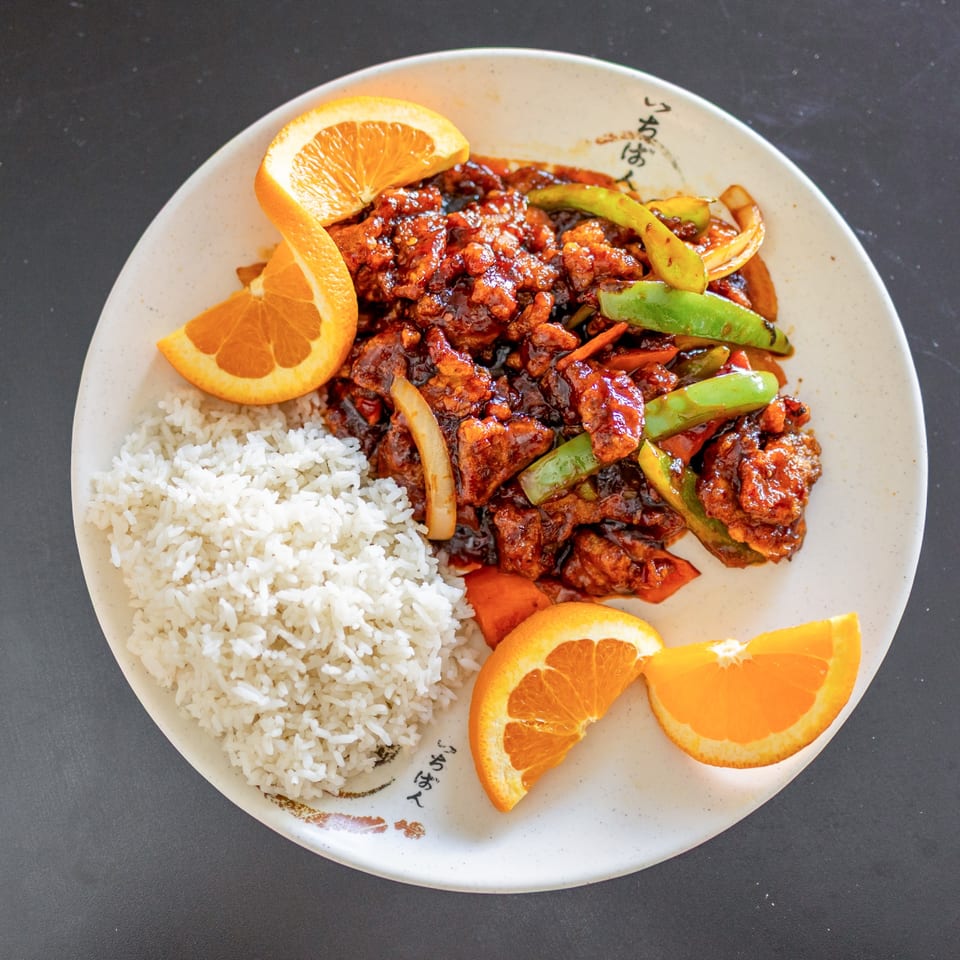 Lover's Eggroll's orange chicken with white rice, bell peppers, and orange slices on a white plate.