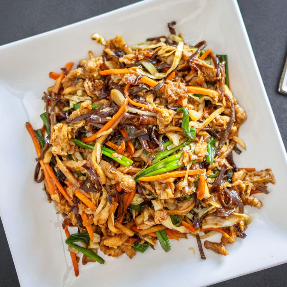 Close-up of a Chinese stir-fry dish with shredded vegetables, mushrooms, and meat on a white plate.