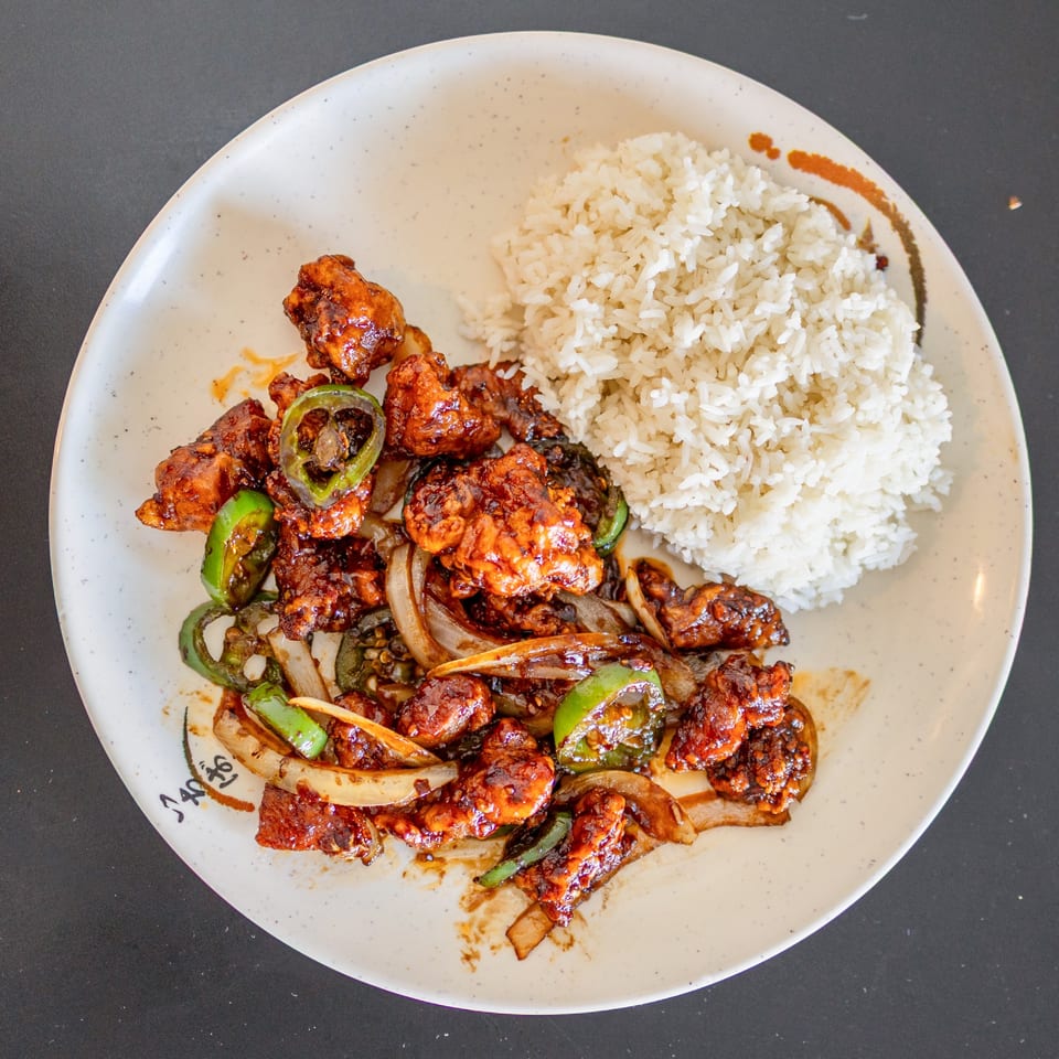 Spicy Lover's Eggroll chicken with green peppers, onions, and white rice on a white plate.