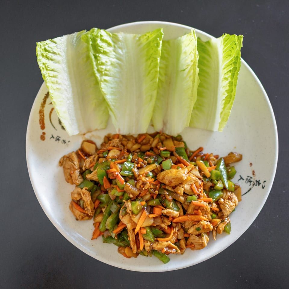 Lover's Eggroll chicken lettuce wraps with green peppers and carrots on a white plate.